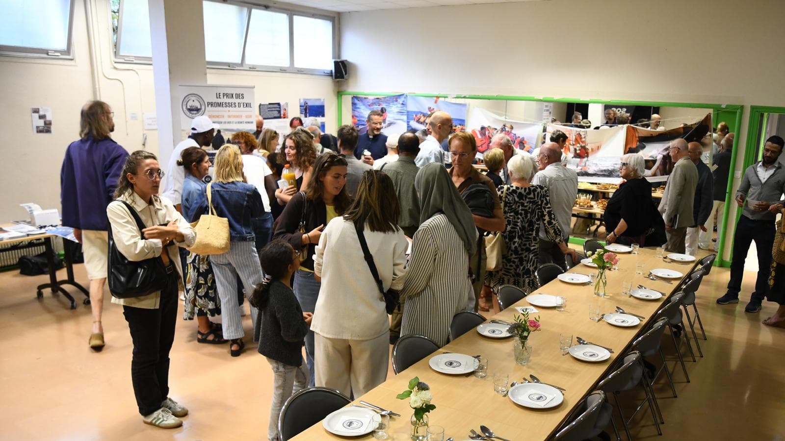 Le public se retrouve dans la salle d'accueil, entre le kakémono de l'association et l'exposition